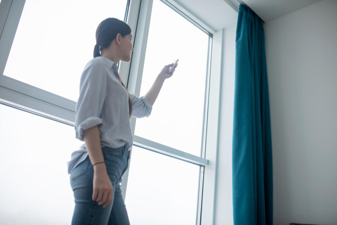 Girl pointing a remote controller at automated window blinds.
