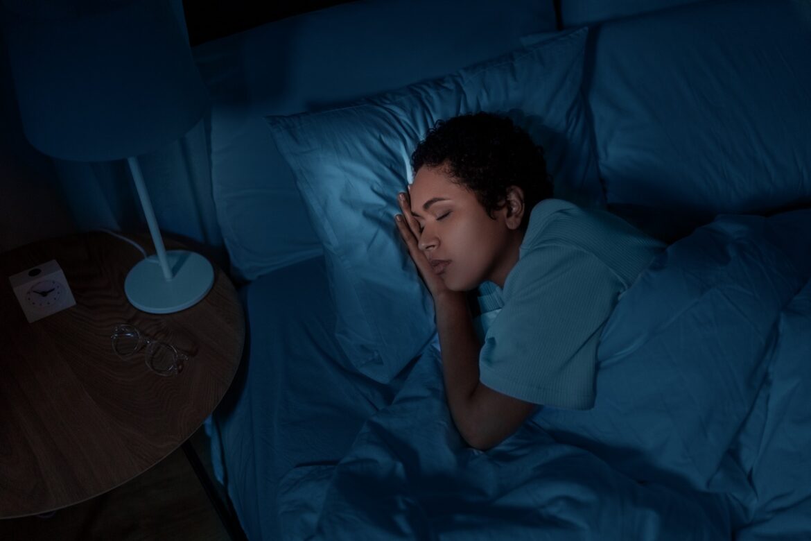 Person sleeping peacefully in a dark bedroom, demonstrating how blackout shades help improve sleep quality